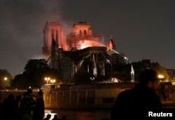 Firefighters douse flames from the burning Notre Dame Cathedral as people look on in Paris, France, April 15, 2019.