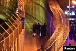 FILE - An African migrant stands on top of a border fence as Spanish police stand guard below during a failed attempt to cross into Spanish territories, between Morocco and Spain's north African enclave of Ceuta, Jan. 1, 2017.
