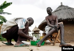 FILE - Apollo Longa-Kenyi (L), a leprosy counseling and care worker, administers topical cream to a blister on Benjamin Longa's foot in Mogiri, south Sudan July 7, 2007.