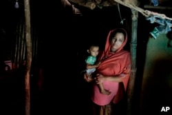 In this Aug. 27, 2018, photo, Rohingya refugee woman Minara Begum, mother of Rahima Akter, holds her youngest daughter Arohi Zannat inside the family hut in Kutupalong refugee camp, Bangladesh.