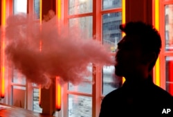 FILE - A customer exhales vapor from an e-cigarette at a store in New York.