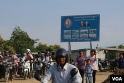 អ្នកធ្វើដំណើរត្រៀមឆ្លងកាត់សាឡាងមួយនៅក្នុងខេត្តកណ្តាល ដើម្បីឆ្លងមករាជធានីភ្នំពេញ។ ស្លាកសញ្ញា​គណបក្សប្រជាជនកម្ពុជាត្រូវបានដាក់​នៅទីនោះ។ (ស៊ុន ណារិន/VOA)