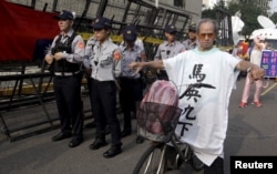 An activist protests against the Singapore meeting between Taiwan's President Ma Ying-jeou and China's President Xi Jinping while police officers stand guard outside the Ministry of Economic Affairs in Taipei, Taiwan, Nov. 7, 2015.