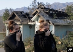 Crystal Shore, left, and her sister Carrie look over the damage to their neighbor's home along Via San Anselmo in the Sylmar area of Los Angeles, Dec. 6, 2017.