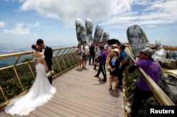 A couple stand near giant hands structure for their wedding photos on Gold Bridge on Ba Na hill near Danang city, Vietnam August 1, 2018. REUTERS/Kham