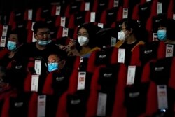 Para pengunjung mengenakan masker untuk menahan penyebaran virus corona, berbincang-bincang sambil menonton film di Poly Cinema di Beijing, China, 25 Februari 2021. (Foto: Andy Wong/Associated Press)