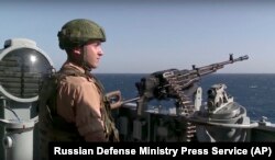 A Russian seaman stands next to a machine gun on the Russian missile cruiser Moskva, near the shore of Syria’s province of Latakia, Nov. 27, 2015.