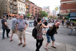 FILE - Steve Grillo, right, bumps elbows with a friend in the Hell's Kitchen neighborhood of New York, Friday, May 29, 2020, during the coronavirus pandemic. Grillo lives on the blocked-off street and is a walking advertisement touting his West Side commu