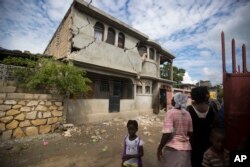 Residents look at a home damaged by a magnitude 5.9 earthquake the night before, in Gros Morne, Haiti, Oct. 7, 2018.