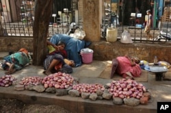 Indian vendors selling onions rest on a sidewalk under the shade of a tree on a hot summer day in Hyderabad, India.