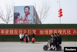 Men ride a scooter past a poster showing Chinese President Xi Jinping on the side of a school building in Henan province, China February 22, 2019.