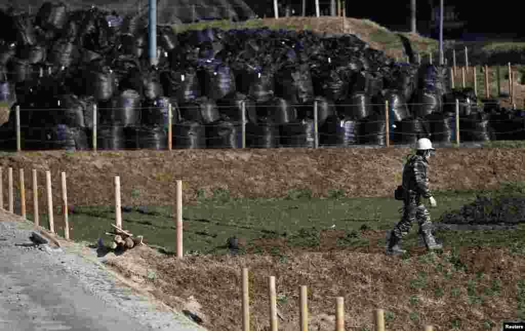 Seorang pria berjalan dekat kantong-kantong plastik sampah yang berisi tanah, daun dan puing-puing yang terkena radiasi dari operasi dekontaminasi di sebuah tempat penyimpanan di wilayah Miyakoji, Tamura di prefektur Fukushima (1/4).
