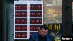 Seorang pria membaca koran di depan kantor penukaran mata uang di Kyiv (10/11). (Reuters/Gleb Garanich)