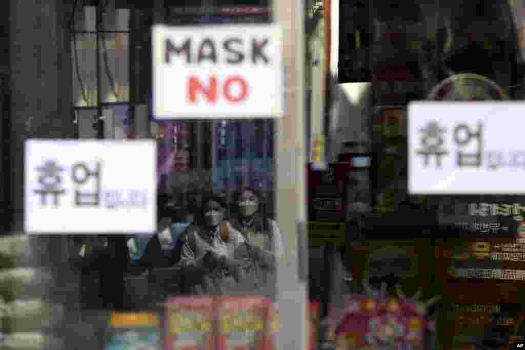 Women wearing a face mask are reflected on a window of a temporarily closed store in Seoul, South Korea, March 18, 2020.