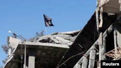 FILE - A flag of Islamic State militants flies above a destroyed house in Raqqa, Syria, Oct. 18, 2017. U.S. authorities will soon release a man with dual U.S.-Saudi citizenship whom they suspect had signed up as an Islamic State fighter in Syria.