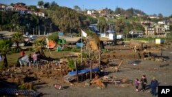People walk past destroyed surfing schools on the beach after an earthquake-triggered tsunami in Concon, Chile, Sept. 17, 2015.