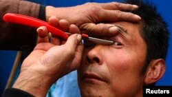 FILE - A barber uses a razor to clean the eyelids of his customer, as a part of his hair shaving service, at a residential area in Suining, Sichuan province, Feb. 23, 2012. 