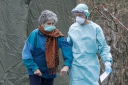 An elderly patient is helped by a doctor at one of the emergency structures that were set up to ease procedures at the Brescia hospital, northern Italy, Thursday, March 12, 2020.