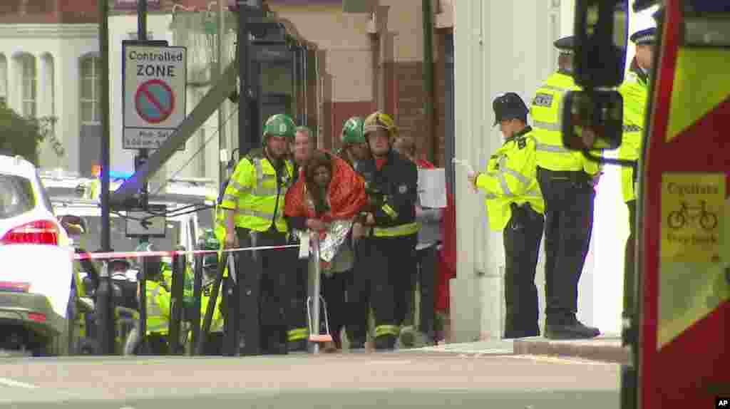 In this image made from video, a woman with blankets wrapped around her is being escorted by emergency services near the scene of an explosion in London Friday, Sept. 15, 2017.