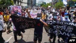 ក្រុម​បាតុករ​នាំ​គ្នា​កាន់​បដា ហើយ​លើក​ម្រាម​ដៃ​បី​ឡើង ក្នុង​អំឡុងពេល​តវ៉ា​ប្រឆាំង​នឹង​រដ្ឋប្រហារ​យោធា​ក្នុង​ទីក្រុង​រ៉ង់ហ្គូន ប្រទេស​មីយ៉ាន់ម៉ា ថ្ងៃទី១២ ខែឧសភា ឆ្នាំ២០២១។ 