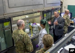 This September 2022, image provided by Los Alamos National Laboratory shows Lt. Gen. Thomas Bussiere, left, and James Owen, right, watch as scientist Bi Nguyen demonstrates the wet slurry formulation process in Los Alamos, N.M. (Los Alamos National Laboratory via AP)
