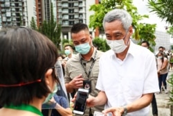 People's Action Party Secretary-General and Singaporean Prime Minister Lee Hsien Loong, right, verifies his identity with a polling official at the Alexandra Primary School polling center in Singapore, July 10, 2020.