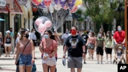 Guests required to wear masks because of the coronavirus pandemic stroll through the Disney Springs shopping, dining and entertainment complex Tuesday, June 16, 2020, in Lake Buena Vista, Fla. Walt Disney World Resort theme parks plan to reopen on July 11