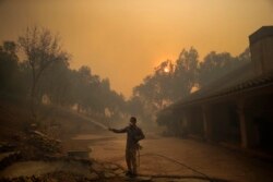 Marco Alcaraz uses a garden hose to protect his girlfriend's home as the Easy fire approaches, Oct. 30, 2019, in Simi Valley, Calif.