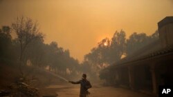 Marco Alcaraz uses a garden hose to protect his girlfriend's home as the Easy fire approaches Wednesday, Oct. 30, 2019, in Simi Valley, Calif.