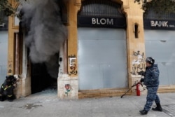 A firefighter looks before entering a bank that was set on fire by anti-government protesters, as a riot policeman passes by, during a protest in Beirut, Lebanon, Feb. 11, 2020.