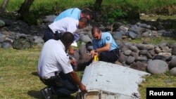 French gendarmes and police inspect a large piece of plane debris which was found on the beach in Saint-Andre, on the French Indian Ocean island of La Reunion, July 29, 2015.