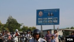 អ្នកធ្វើដំណើរត្រៀមឆ្លងកាត់សាឡាងមួយនៅក្នុងខេត្តកណ្តាល ដើម្បីឆ្លងមករាជធានីភ្នំពេញ។ ស្លាកសញ្ញា​គណបក្សប្រជាជនកម្ពុជាត្រូវបានដាក់​នៅទីនោះ (ស៊ុន ណារិន/VOA)