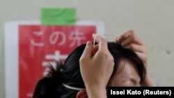 Seorang pekerja medis mencoba untuk melepas masker pelindung wajah di bangsal Intensive Care Unit (ICU) untuk pasien Covid-19 di Rumah Sakit Universitas Kedokteran St. Marianna di Kawasaki, selatan Tokyo, Jepang, 4 Mei 2020. (Foto: REUTERS/Issei Kato)