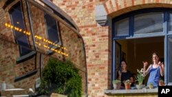 A woman responds from a window as a bus delivers a loudspeaker message from family and friends in Brussels, Wednesday, April 22, 2020. (AP Photo/Olivier Matthys)