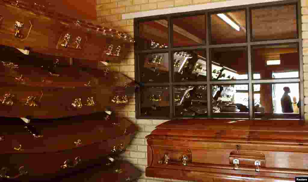 Coffins are displayed as a worker is reflected in a window at the Sizo funeral parlor in Soweto, South Africa, May 6, 2013.