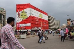 Venders and protesters gather under a mural urging the peaceful overthrow of the government in Nour Square in Tripoli, Lebanon, Nov. 15, 2019. (Heather Murdock/VOA)