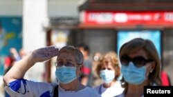 FILE - A woman wearing a protective face mask salutes as people hold a minute of silence during the last day of the official ten-day mourning of those who died of the coronavirus disease (COVID-19), at Puerta del Sol square in Madrid, June 5, 2020. 
