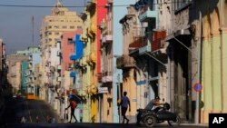 FILE - A man pushes his motorcycle as people walk on the freshly painted buildings along Reina Street in Havana, Cuba, Sept. 19, 2015. 