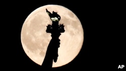 In this July 31, 2015, file photo, a full moon rises behind the torch of the Statue of Liberty as seen from Liberty State Park in Jersey City, N.J. But what does it mean "to carry a torch for someone"? Read on to find out! (AP Photo/Julio Cortez)