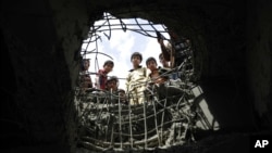 FILE - Boys look through a hole made by a Saudi-led airstrike on a bridge in Sana'a, Yemen, March 23, 2016.