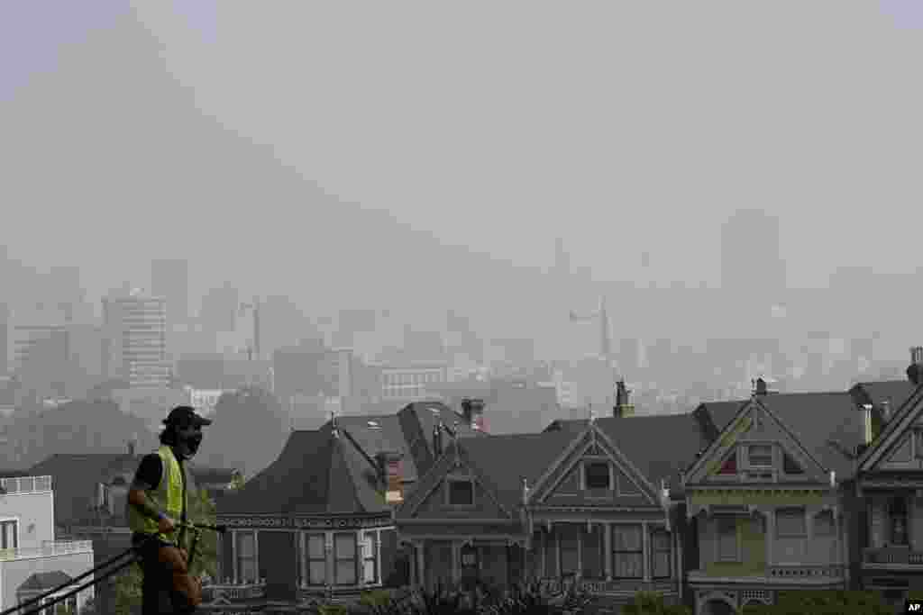 កម្មករម្នាក់កំពុងសម្អាតស្មៅនៅសួន Alamo Square ខណៈផ្សែងដែលបណ្តាលមកពីភ្លើងឆេះព្រៃនិងអាប់ពេលព្រឹក កំពុងគ្របដណ្តប់បរិយាកាសនៅទីក្រុង San Francisco រដ្ឋ California កាលពីថ្ងៃទី ១៤ ខែកញ្ញា ឆ្នាំ២០២០។