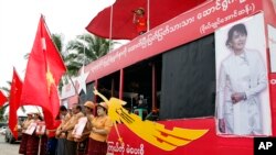 អ្នក​គាំទ្រ​ដែលកាន់​ទង់​គណបក្ស​សម្ព័ន្ធ​ជាតិ​ប្រជាធិបតេយ្យ​របស់​លោក​ស្រី អោង​ សានស៊ូជី ឈរ​នៅជិត​ក្រុមអ្នក​ចម្រៀង​ដែល​ច្រៀង​នៅ​លើ​ឡាន​ឃោសនា​បោះឆ្នោត​នៅ​ក្នុង​ទីក្រុង​ Yangon ប្រទេស​ភូមា​ កាលពីថ្ងៃទី៧ ខែតុលា ឆ្នាំ២០១៥។