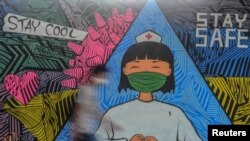 Seorang pejalan kaki berjalan dekat mural yang menggambarkan seorang perawat sebagai tanda dukungan kepada para medis yang menjadi garda terdepan penanganan wabah virus corona (COVID-19) di Ciamis, Jawa Barat, 10 April 2020, sebagai illustrasi. (Foto: Reuters)
