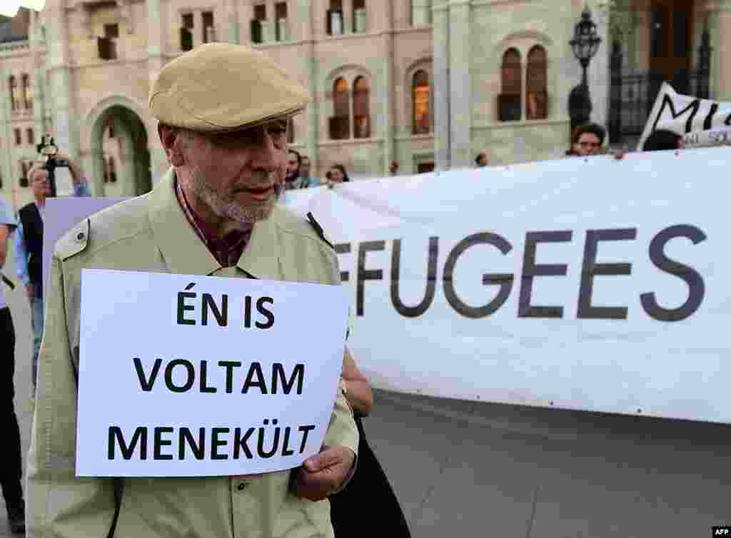 An elderly man walks with his placard with text, "I was refugee also," as activists hold up a banner with 'Refugees welcome' during protests against the migration policy of the Orban government in front of the parliament building in Budapest, Sept. 30, 20
