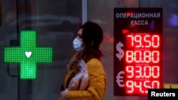 FILE - Woman walks past a board showing currency exchange rates of the euro and U.S. dollar against the Russian rouble in Moscow, Nov. 2, 2020.