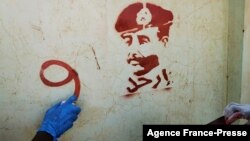 FILE - A person sprays graffiti next to a stencil painting of the Sudan's top army general, Abdel Fattah al-Burhan, with writing in Arabic that reads "leave," during a protest in Khartoum, Nov. 4, 2021, against a widely condemned military takeover.