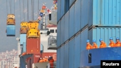 Workers look at cranes lifting containers onto cargo vessels at a port in Yantai, Shandong province, China October 17, 2019. 