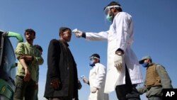FILE - In this March 22, 2020 photo, health workers measure the temperature of Afghan passengers in an effort to prevent the spread of the coronavirus, as they enter Kabul trough Kabul's western entrance gate, in the Paghman district of Kabul.