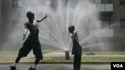 Panas yang sangat menyengat membuat dua anak di Washington DC bermain sambil mandi air dari pipa pemadam kebakaran (21/7).