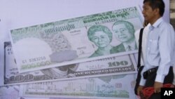 FILE - Cambodian men hang out by a currency poster during the inauguration ceremony of the Cambodia Securities Exchange in Phnom Penh, Cambodia, Monday, July 11, 2011.